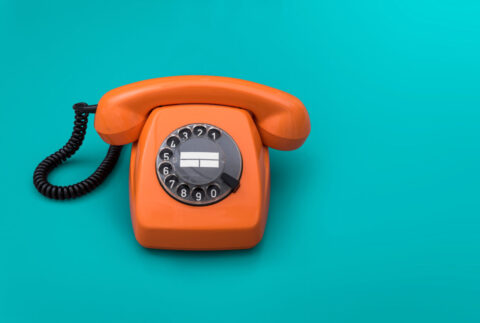 Telefono fisso arancione vintage con disco combinatore su sfondo turchese.