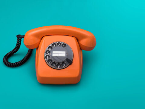 Telefono fisso arancione vintage con disco combinatore su sfondo turchese.